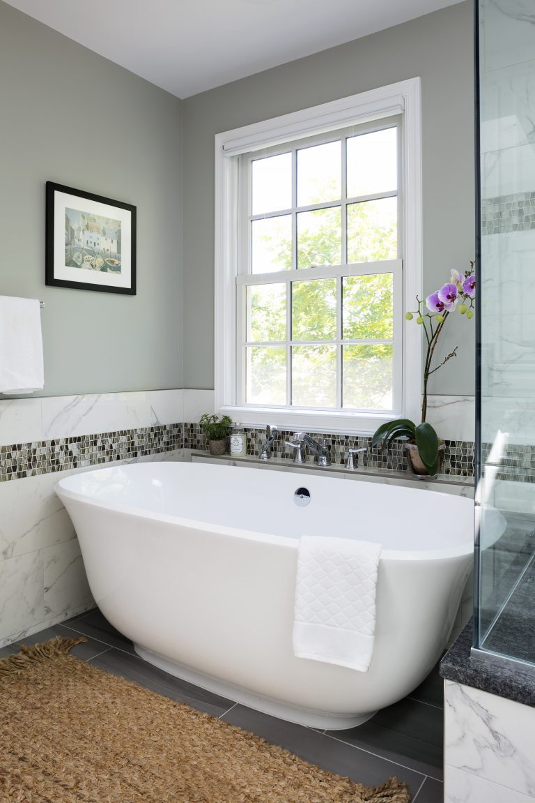 freestanding tub under window natural color palette white beige and green tile stripe detail