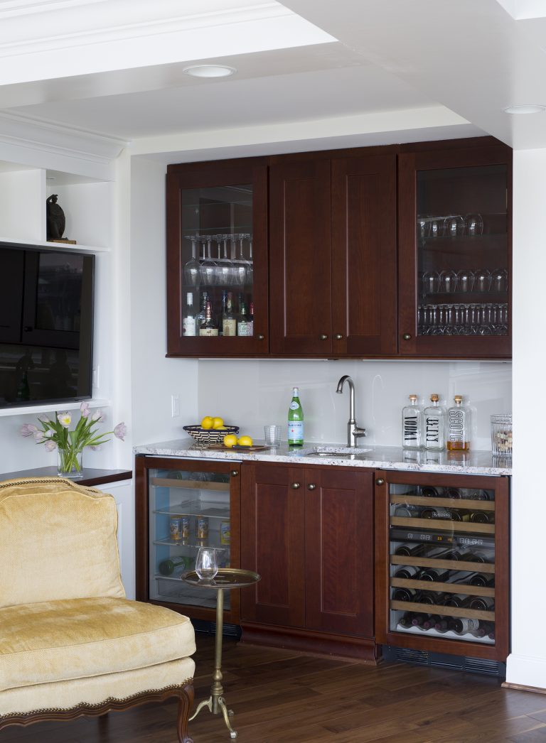 built in bar in living area dark wood cabinetry glass door uppers sink and beverage refrigerators