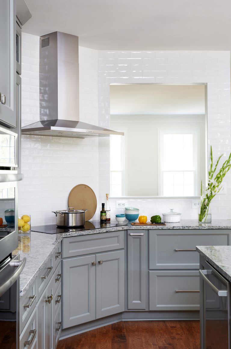 kitchen with wood floors gray cabinetry passthrough to living area white backsplash tile to ceiling stainless steel appliances