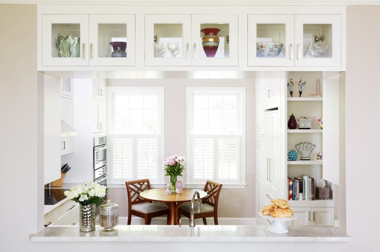 bright white kitchen passthrough into dining area with upper glass door cabinetry