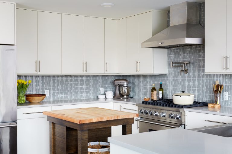 kitchen with white cabinetry gray countertops natural wood island soft blue geometric tile backsplash stainless steel appliances