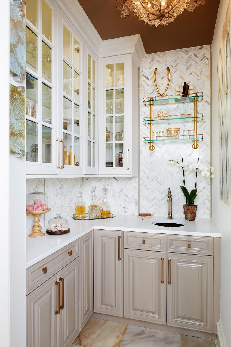 kitchen with gray lower cabinetry white upper cabinetry with glass doors bronze ceiling bronze and gold fixtures and hardware open glass shelving