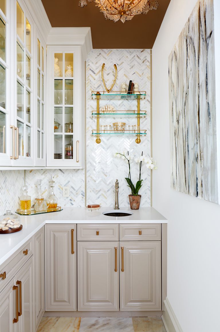 kitchen with gray lower cabinetry white upper cabinetry with glass doors bronze ceiling bronze and gold fixtures and hardware open glass shelving