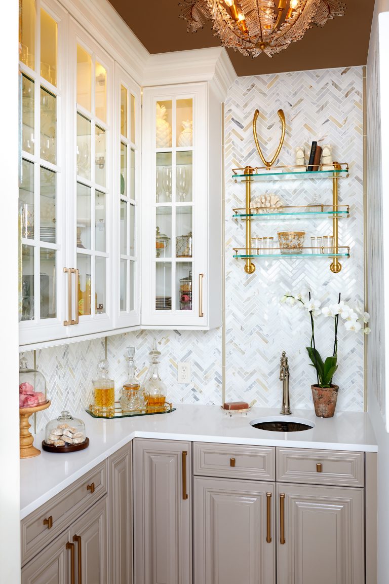 kitchen with gray lower cabinetry white upper cabinetry with glass doors bronze ceiling bronze and gold fixtures and hardware open glass shelving