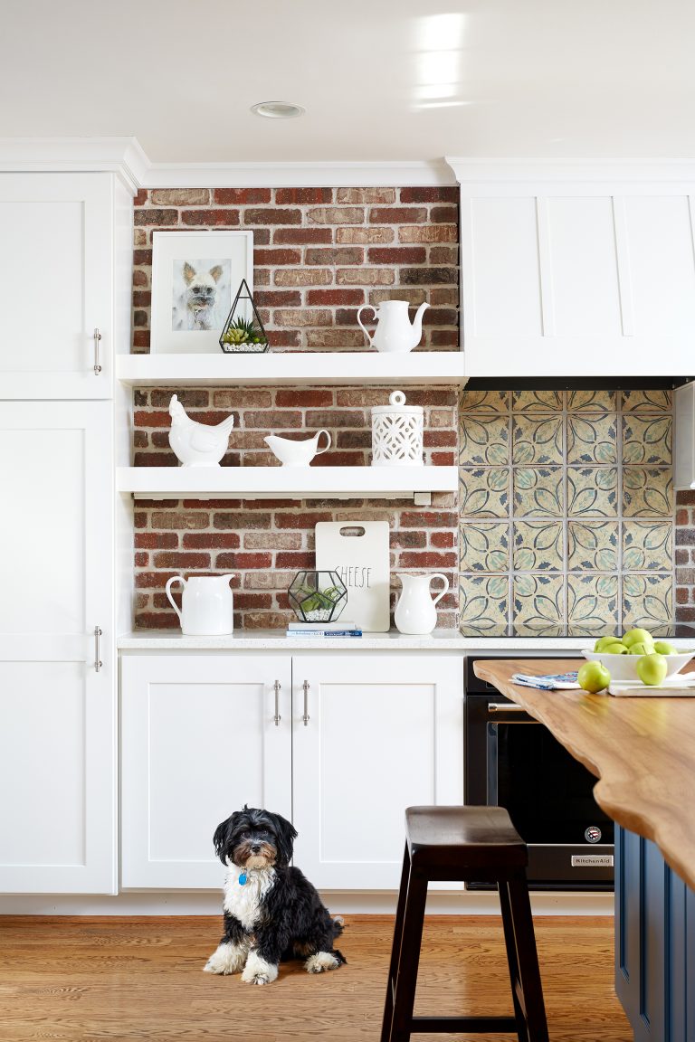 exposed brick wall behind white cabinetry and floating shelves