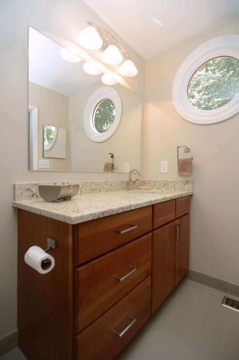 bathroom with medium stained wood vanity lots of counter space large mirror sconce lighting round window