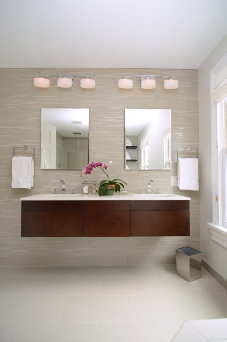 modern bathroom with dark wood floating vanity with double sinks and sconce lighting against tiled feature wall