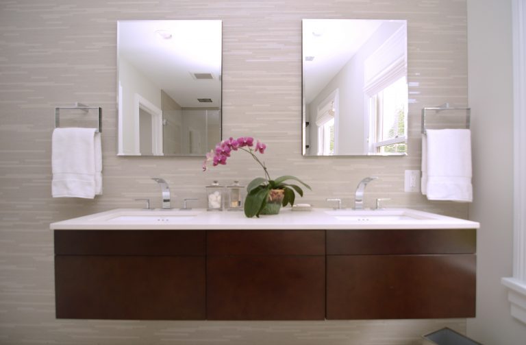 modern bathroom with dark wood floating vanity with double sinks and sconce lighting against tiled feature wall