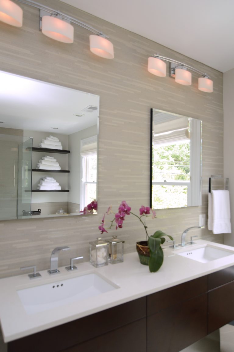 modern bathroom with dark wood floating vanity with double sinks and sconce lighting against tiled feature wall