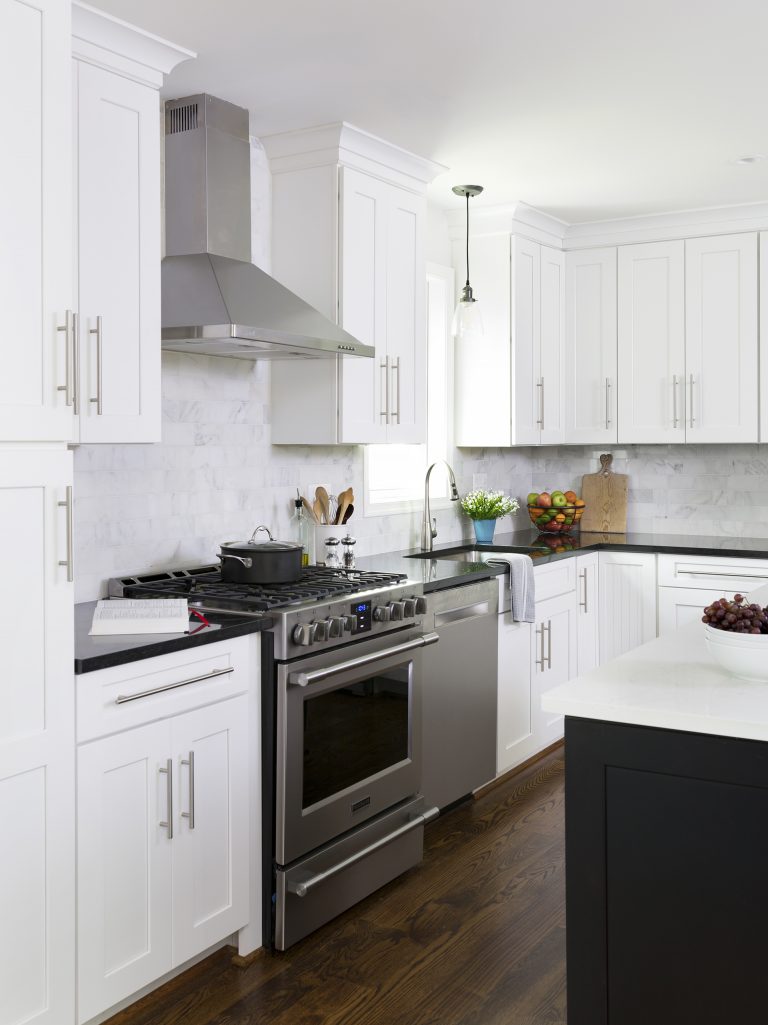 stainless steel gas range and hood white cabinetry black countertops