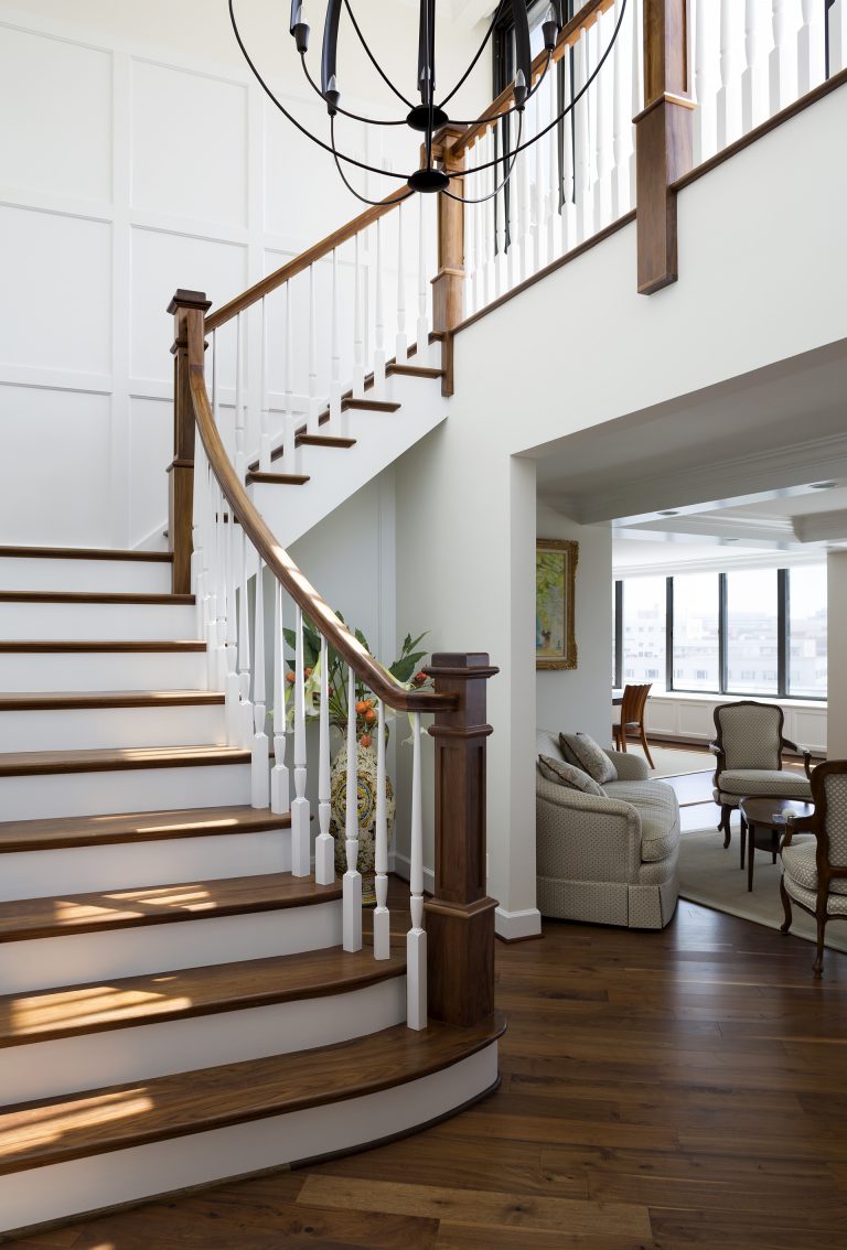 staircase with wooden banister white paneled walls and eclectic chandelier