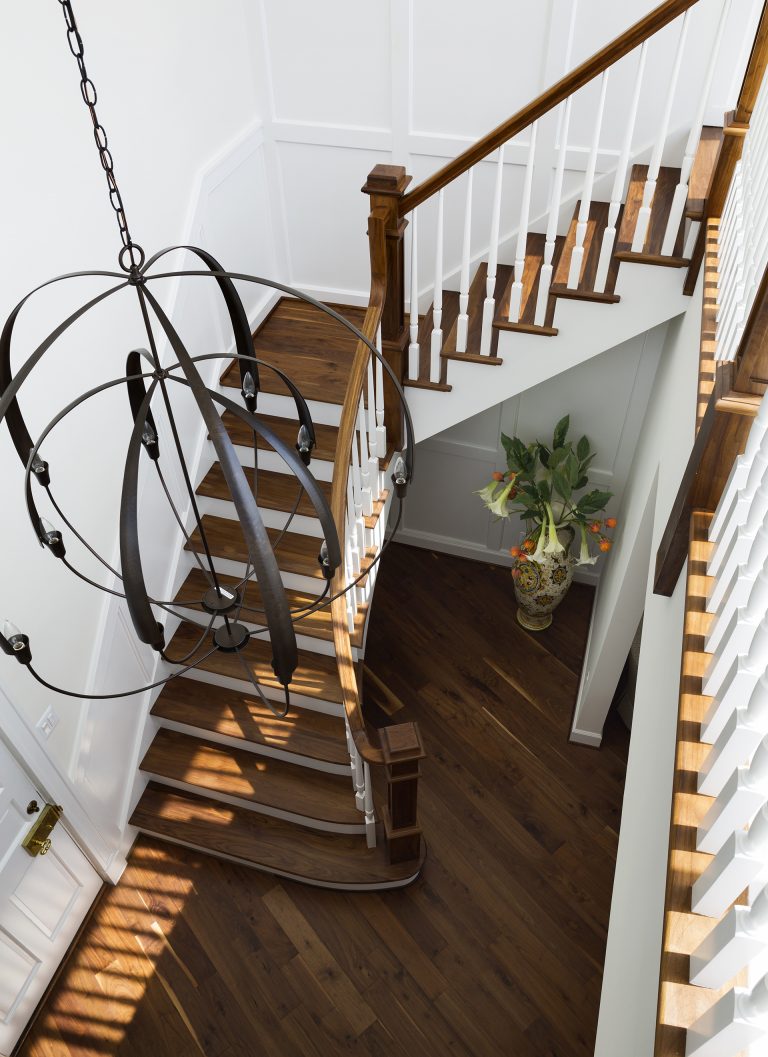 birds eye view of staircase with wooden banister white paneled walls and eclectic chandelier