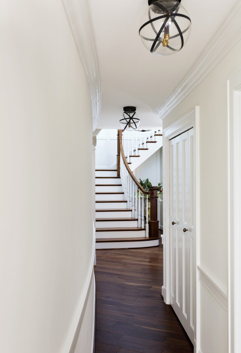 view down hallway into main entryway with staircase white walls dark wood floors eclectic light fixtures