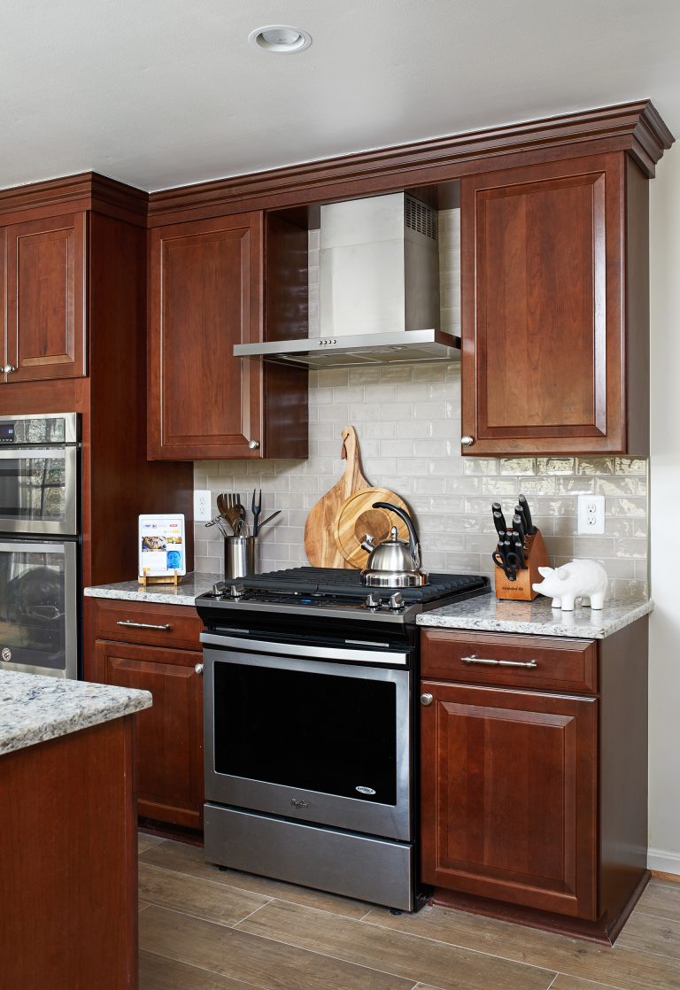 dark stained wood cabinetry stainless steel gas range and hood white subway tile backsplash