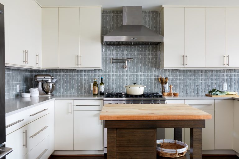 kitchen with white outer cabinets natural wood island geometric backsplash stainless steel gas range and hood