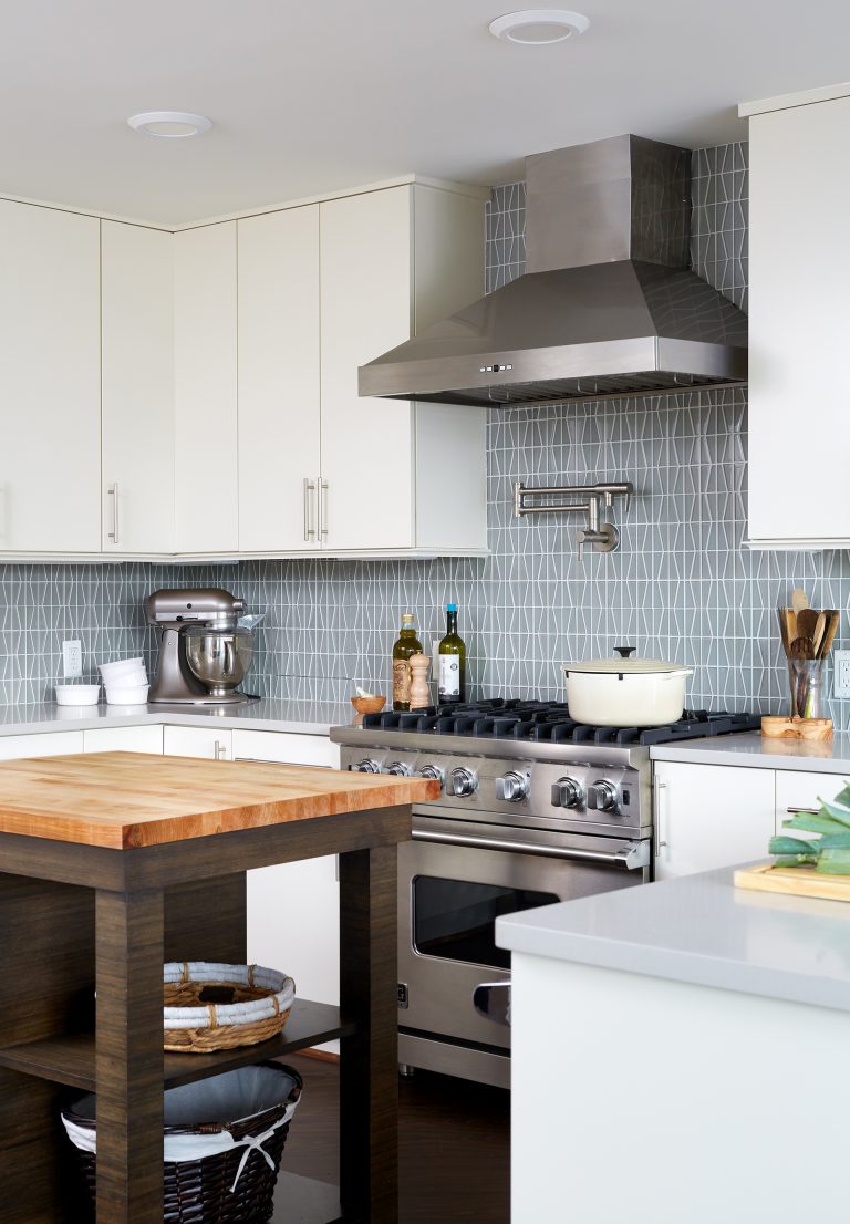 kitchen with white outer cabinets natural wood island geometric backsplash stainless steel gas range and hood