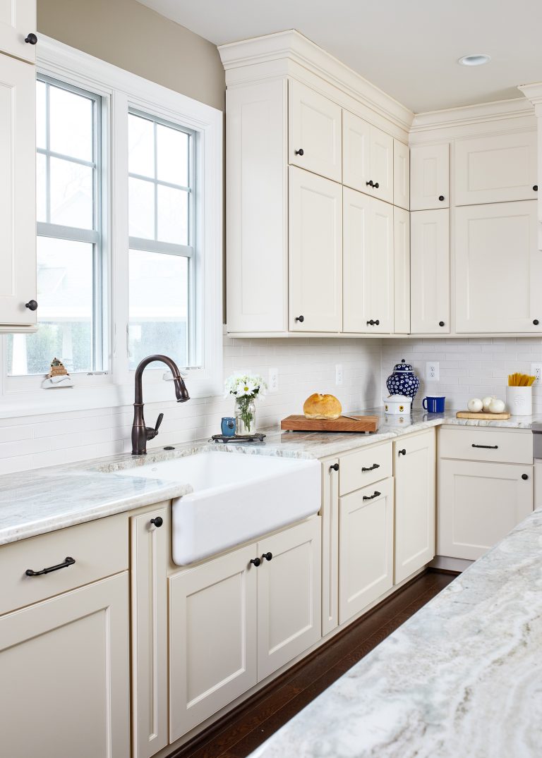 kitchen with cream cabinets porcelain farmhouse sink with bronze fixtures in front of window