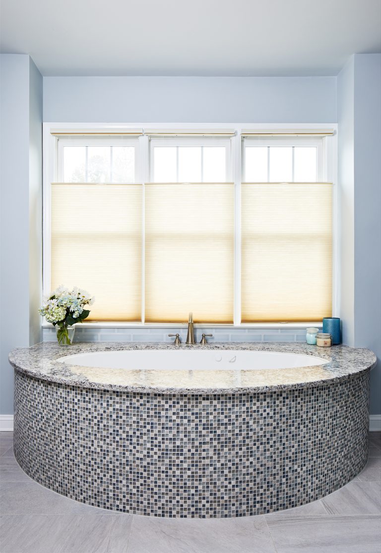 large bathtub with mosaic tile in front of window soft blue walls