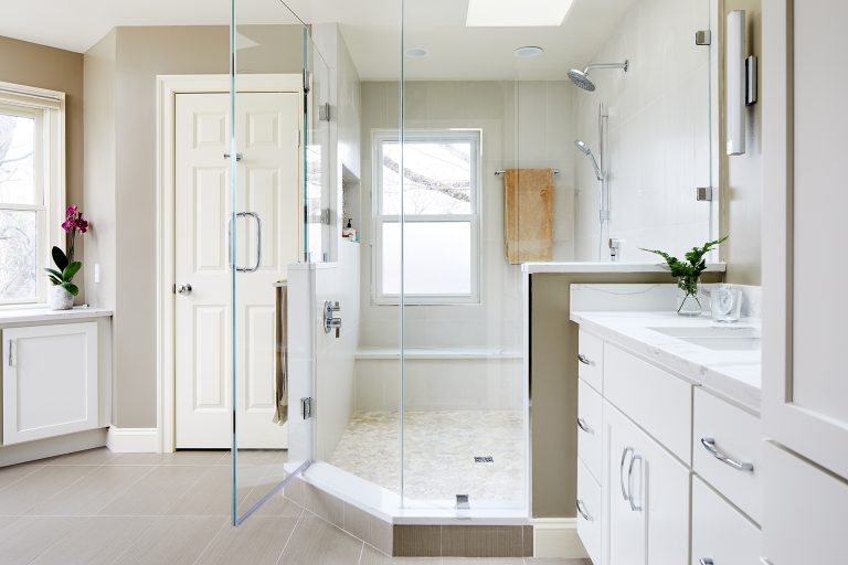 master bathroom renovation white color palette large shower with glass door window skylight and storage nooks built into walls white cabinetry plenty of storage