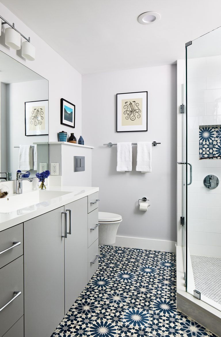 white bathroom with blue and black patterned tile on floors and storage nook