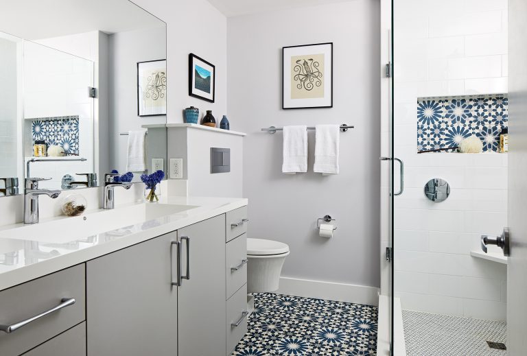 white bathroom shower with glass door and blue accent tile in nook