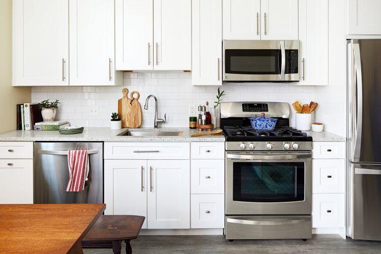 white cabinetry stainless steel gas range and overhead microwave white subway tile backsplash