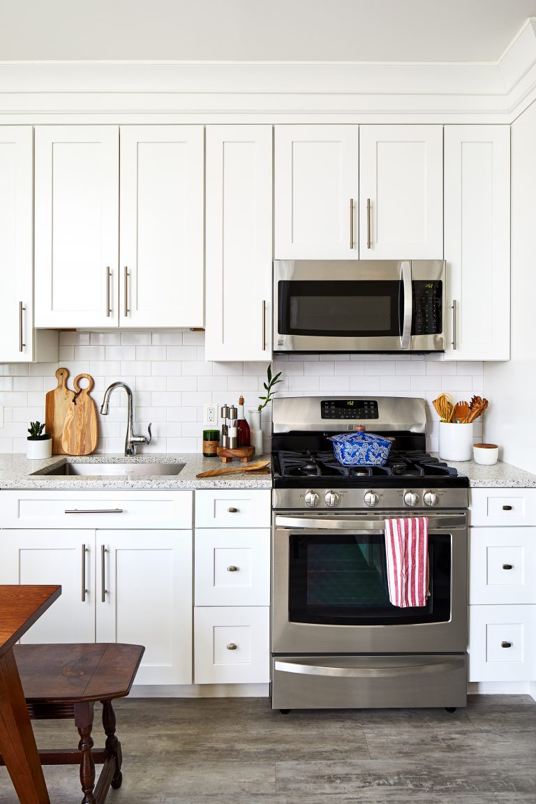 white cabinetry stainless steel gas range and overhead microwave white subway tile backsplash