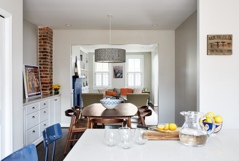 view from kitchen into dining and living area white cabinetry and exposed brick column