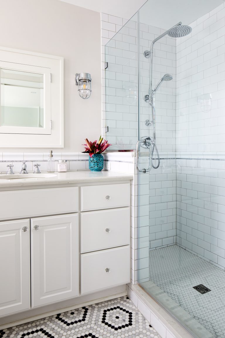 vanity with white cabinetry and sconce lighting shower with white subway tiling and glass door