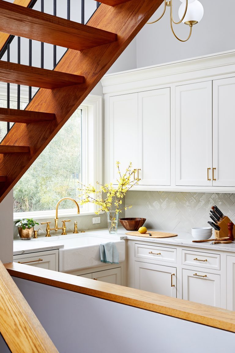 view through open staircase of kitchen white cabinets gold fixtures and hardware