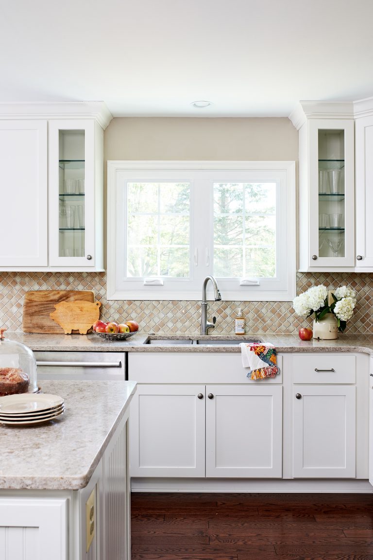 kitchen with white cabinetry and dark wood floors window behind sink glass doors on upper cabinets