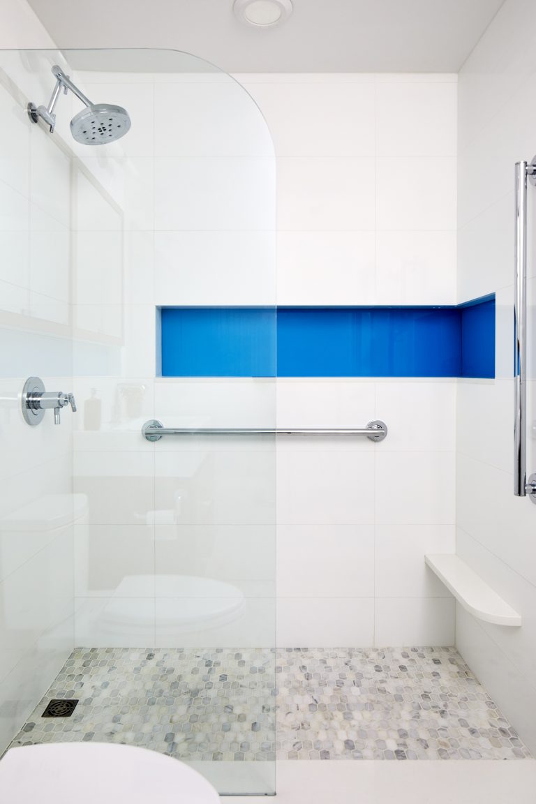 walk in shower with single setting metal rain shower head and built in bench grab bar and storage nook with blue accent tile