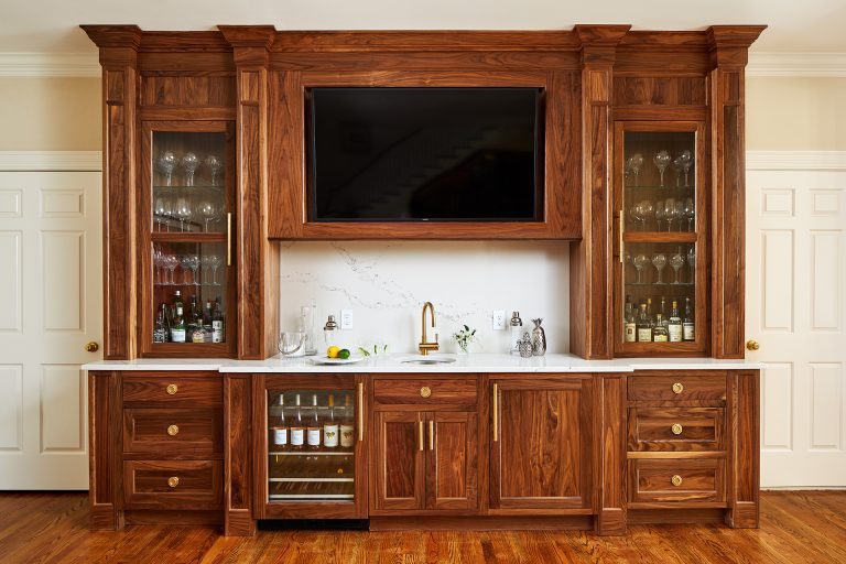 Wet bar with tv above and wood cabinets, wine fridge and sink