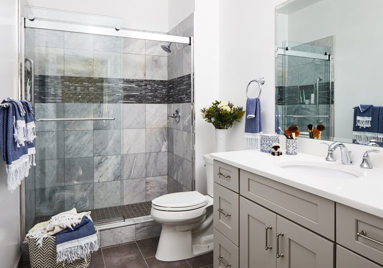 case design bathroom with sliding shower door, double wide mirror, grey cabinets with pull handles