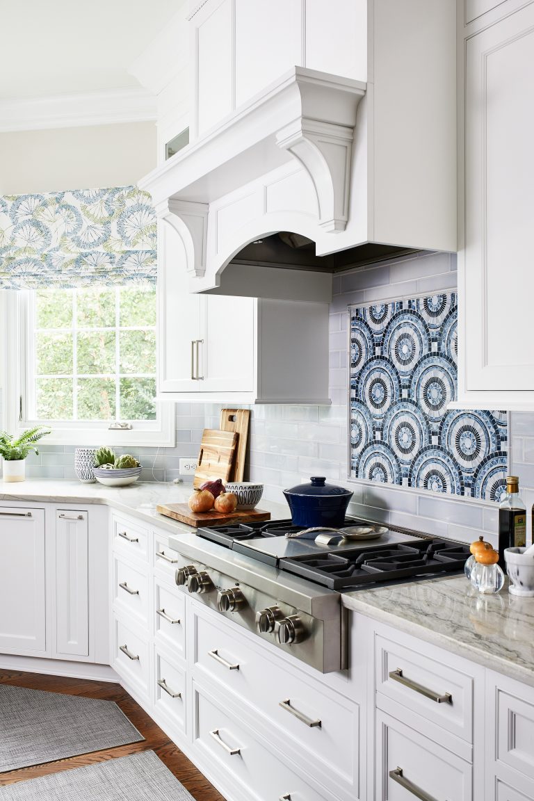 kitchen white panel hood by large window paired with marble countertop and under cooktop drawers with pull handles