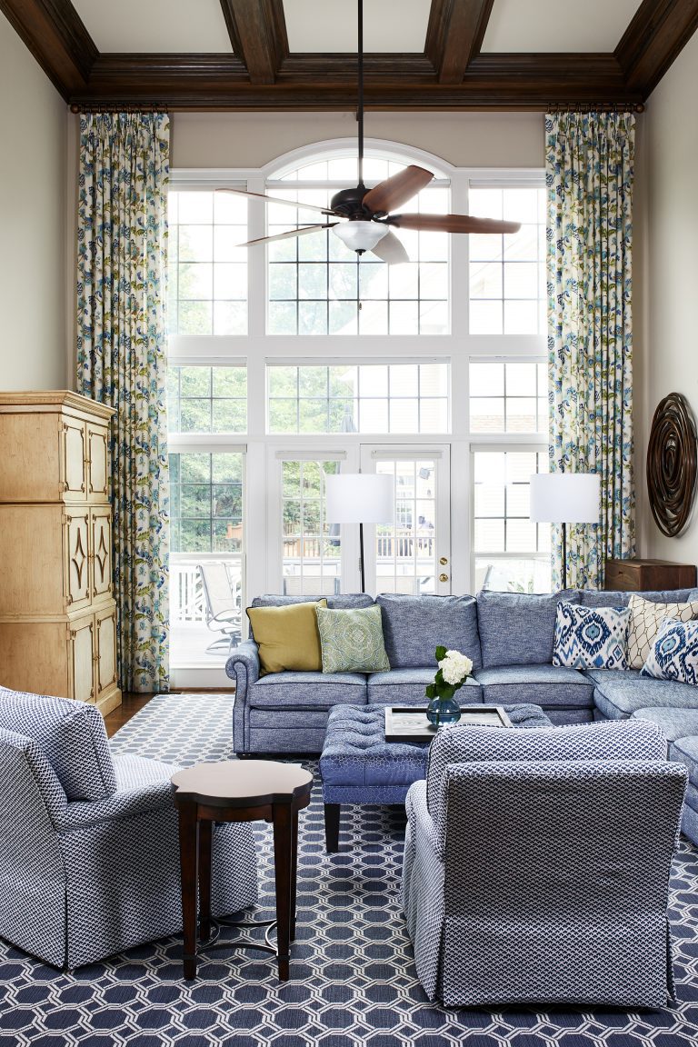 white and blue couches with two story windows, wooden ceiling fan with light and two floor lamps white shades