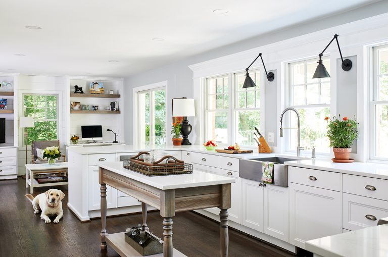 maryland home renovation kitchen with two lamps wall light fixtures with farmhouse apron sink, band of windows over farmhouse sink with polished nickel gooseneck faucet mounted above white cabinets and drawers with pull handles.