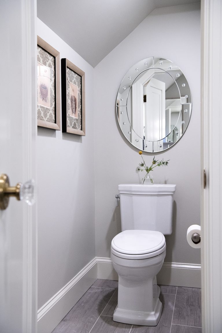 small transitional bathroom with grey walls, grey tiles flooring with oval mirror above toilet