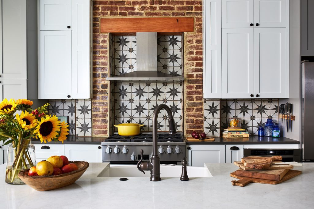 Thin brick arch surround around the cooktop with a tile backsplash and stainless-steel hood range