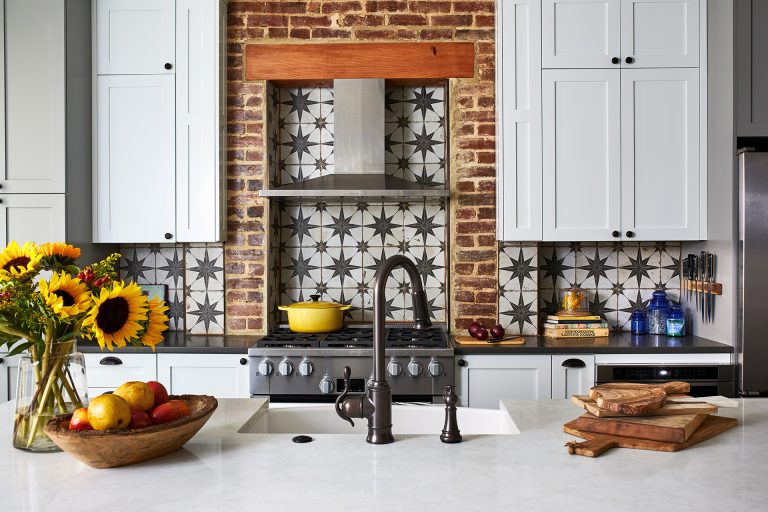 Thin brick arch surround around the cooktop with a tile backsplash and stainless-steel hood range