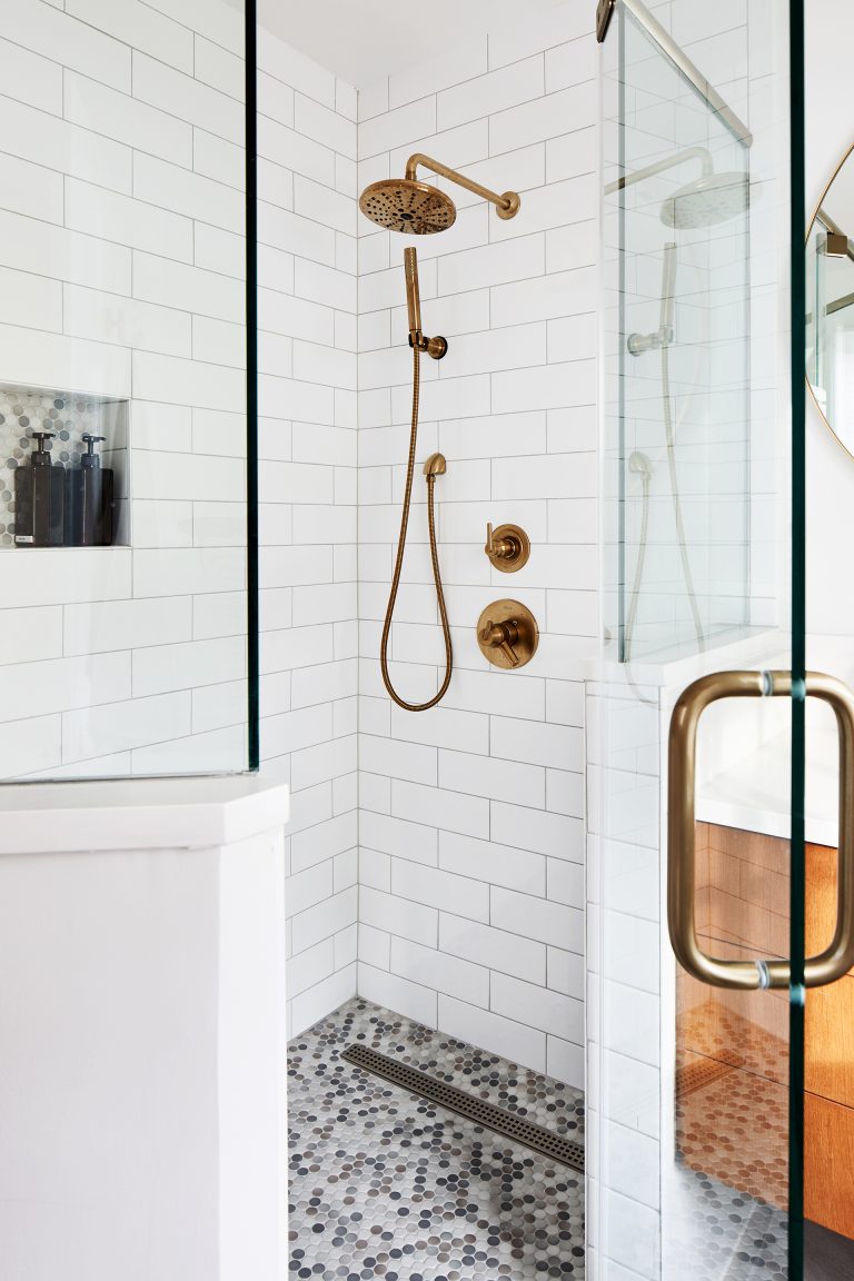 Walk in shower with glass shower door and gold fixtures against white brick tiles