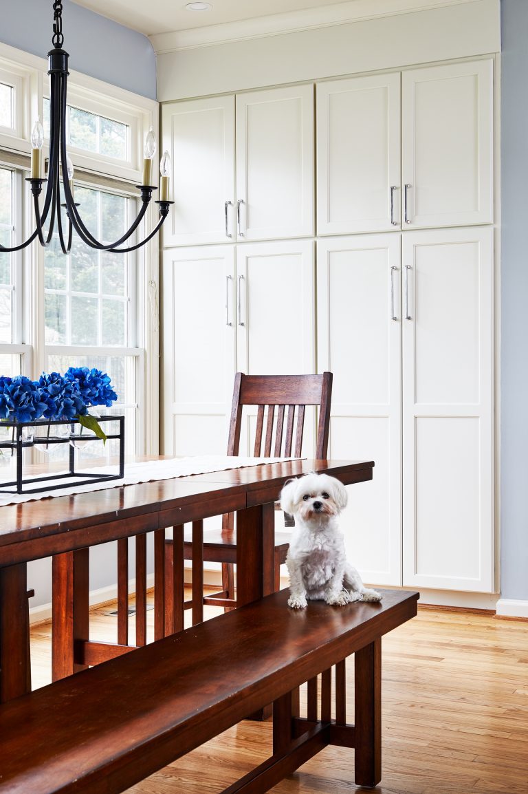 large wooded table with chair and bench, tall white built in cabinets