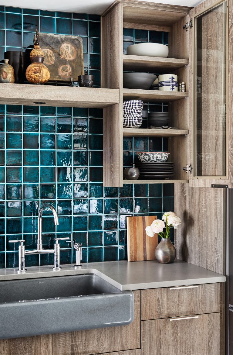 close up of sink with teal tile backsplash and glass door cabinetry and open shelving