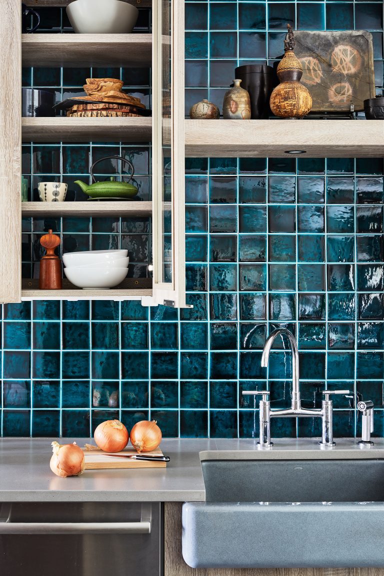close up of sink with teal tile backsplash and glass door cabinetry and open shelving