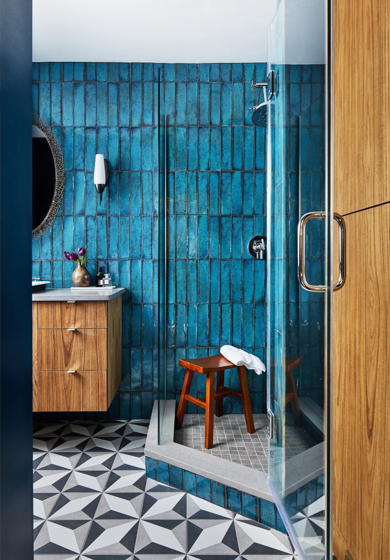 renovated bathroom with geometric tile floor shower stall with glass door teal wall tiling and natural wood floating vanity