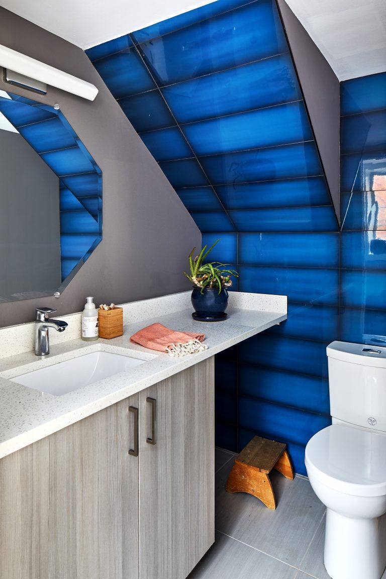 modern renovated bathroom with gray walls and cabinetry white vanity countertops slanted ceiling with blue statement tile