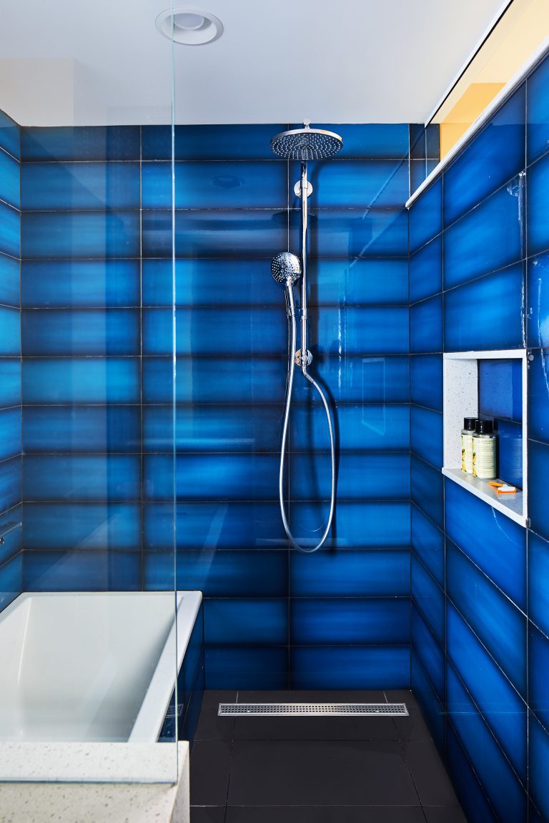 bathtub in shower stall with glass door storage niche and blue tile