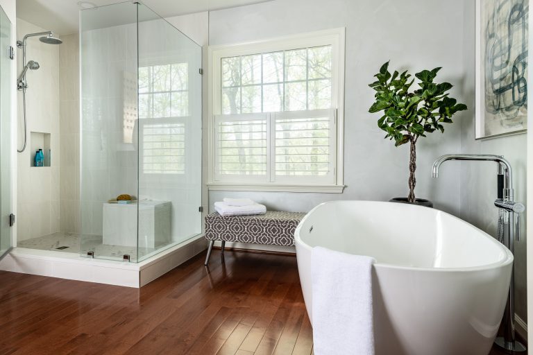 white large freestanding tub, hard wood floors, walk-in shower with rain shower head glass frameless doors with a window view
