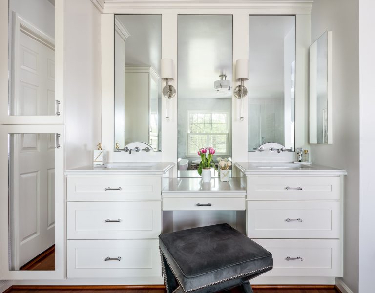 stunning master bathroom with white cabinets with white marble countertops flanking drop-down makeup vanity paired luxury stool and frameless mirrors