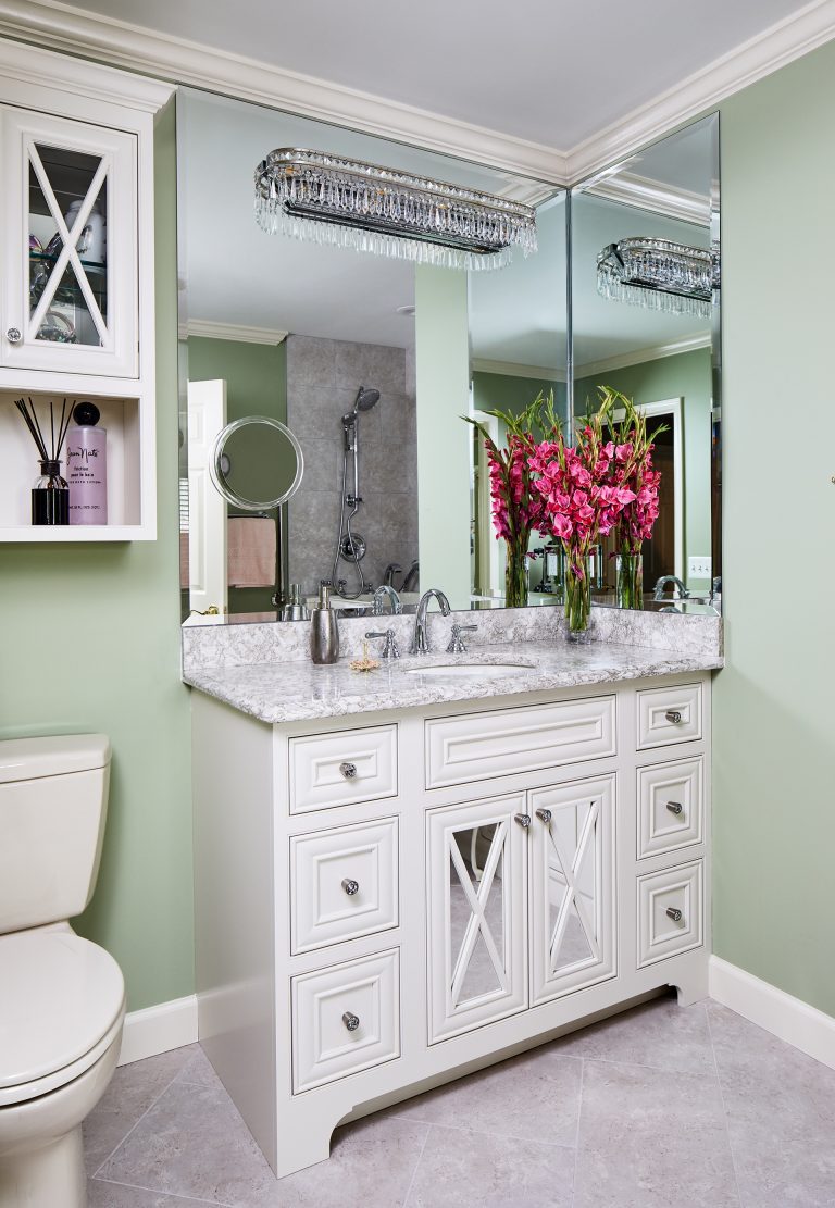 bathroom vanity with square mirror with crystal light fixture and small toilet above two glass doors